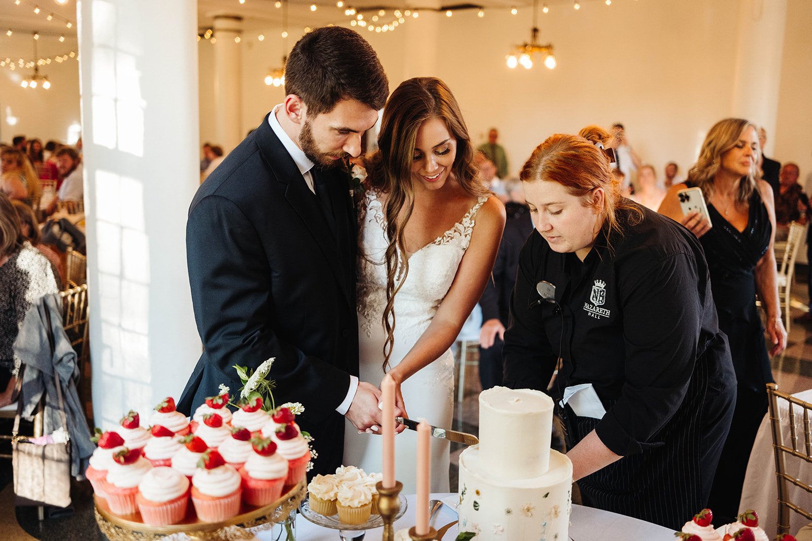 hostess helping the bride and groom cut the wedding cake for the wedding reception